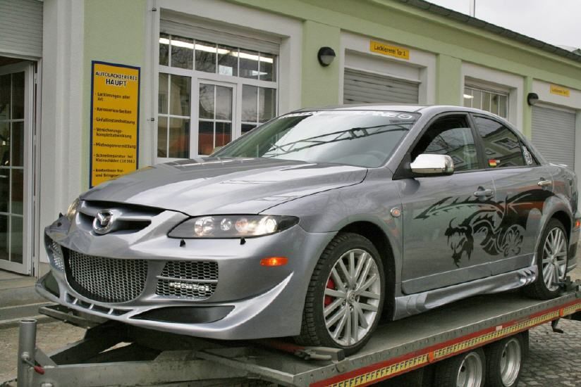 Silberne Sportlimousine auf einem Autotransporter vor einem Gebäude