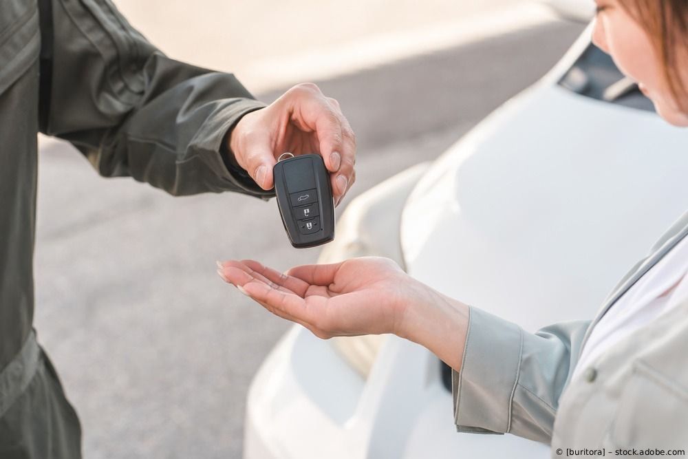 Ein Auto wird in einer Werkstatt mit glänzendem schwarzen Lack lackiert, in der Nähe befinden sich abgeklebte Karosserieteile.