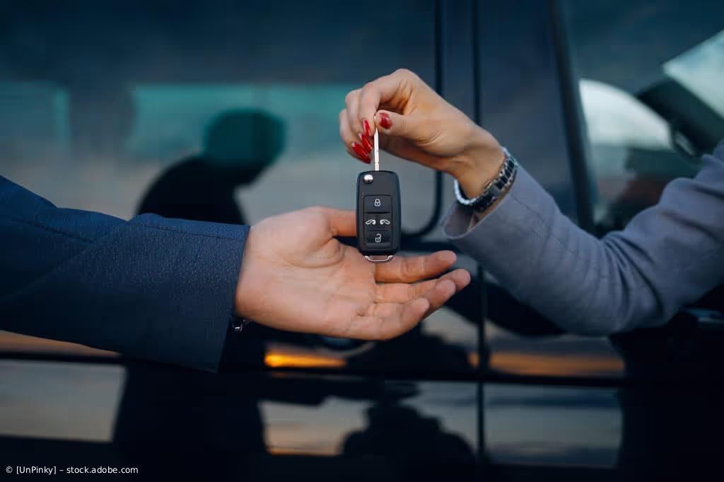Hände tauschen vor einem schwarzen Fahrzeug Autoschlüssel aus.