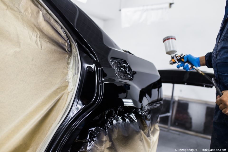 Ein Auto wird in einer Werkstatt mit glänzendem schwarzen Lack lackiert, in der Nähe befinden sich abgeklebte Karosserieteile.