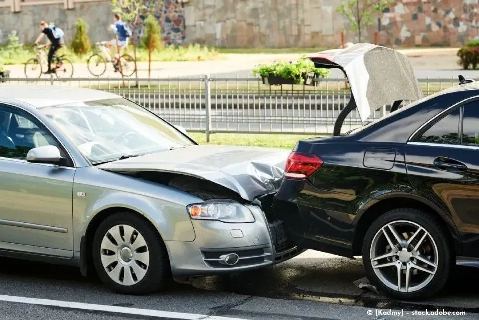 Ein silberner Pkw fuhr auf der Straße in ein schwarzes Auto hinein; Motorhaube und Stoßstange wurden beschädigt.