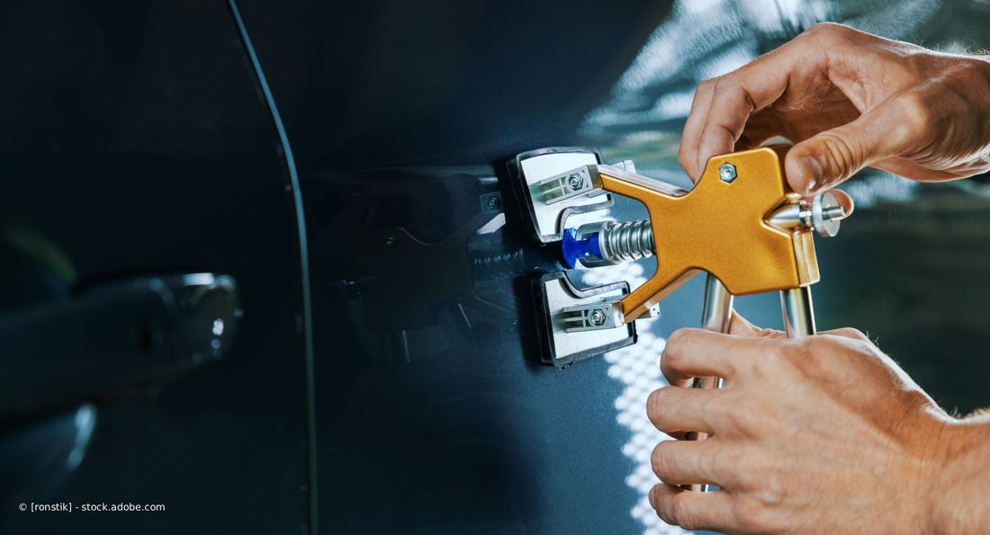 Ein Auto wird in einer Werkstatt mit glänzendem schwarzen Lack lackiert, in der Nähe befinden sich abgeklebte Karosserieteile.