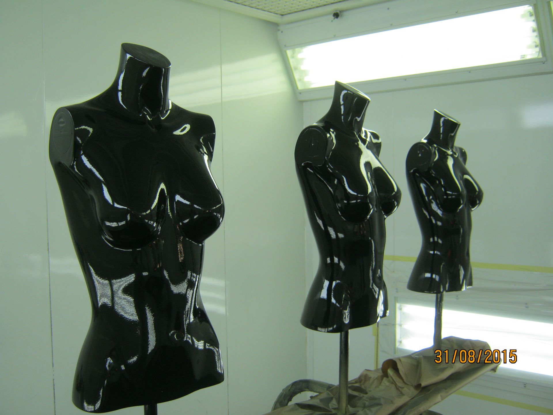 Drei glänzend schwarze Schaufensterpuppen in einem hellen Raum, aus einem bestimmten Winkel betrachtet.