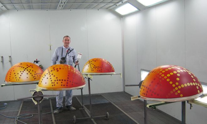 Ein Mann im Laborkittel steht inmitten großer, orange-rot gepunkteter Kuppelstrukturen in einem weißen Testraum.