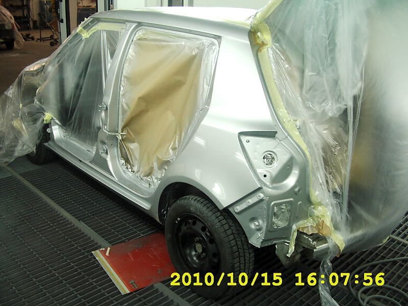 Silberne Autokarosserie in einer Lackiererei, während der Neulackierung mit Plastikfolie abgedeckt und die Fenster abgeklebt.