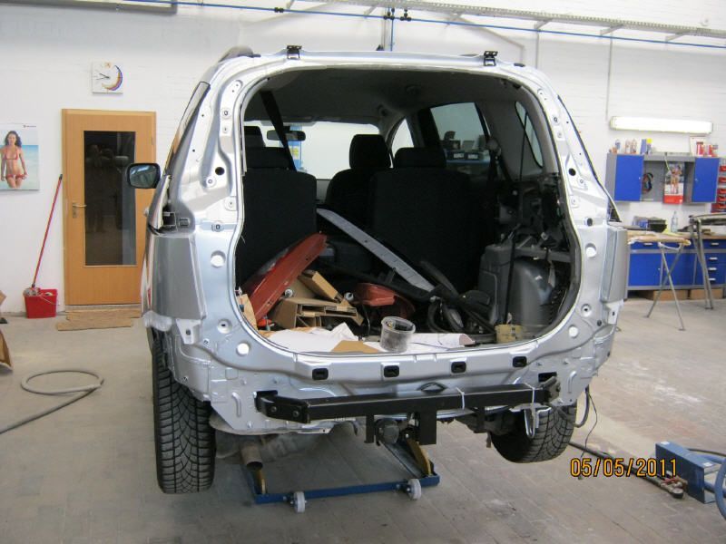 Silberner Transporteraufbau in einer Reparaturwerkstatt, der hintere Innenraum ist ausgebaut und auf einer Hebebühne freigelegt.