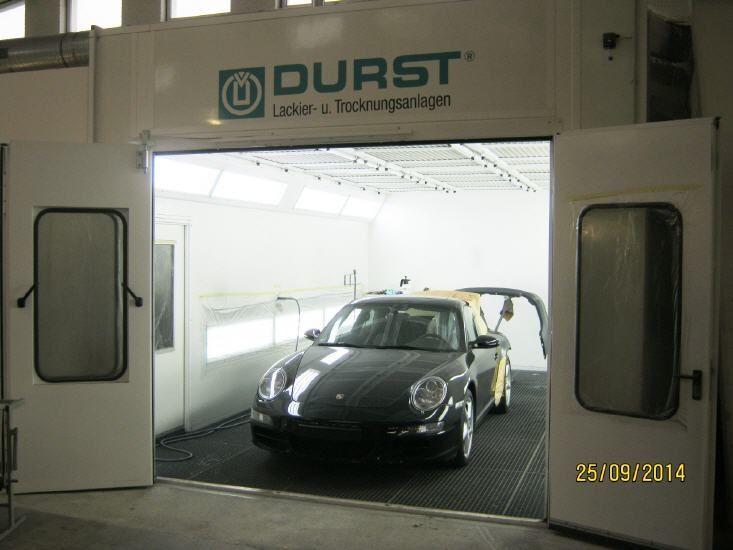 Schwarzer Sportwagen in einer weißen Industrielackierkabine mit PURST-Schild über dem Eingang
