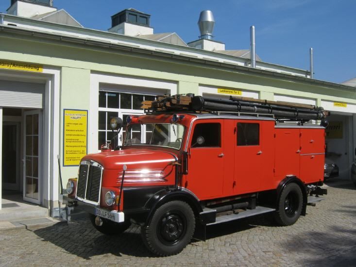 Ein rotes Feuerwehrauto parkt an einem sonnigen Tag vor einem Feuerwehrgebäude.