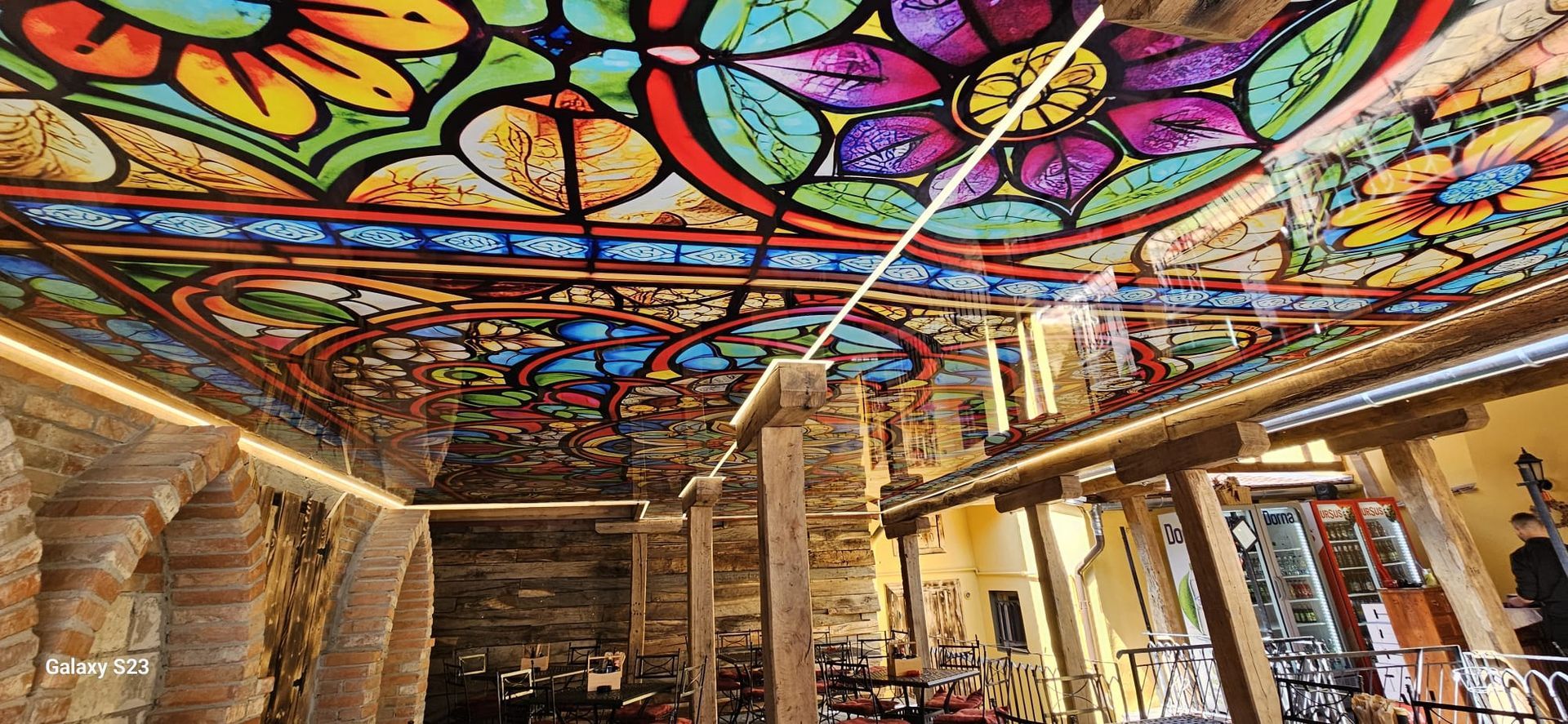 Modernes Wohnzimmer mit grauer Eckcouch, orangefarbenen Stühlen und einer reflektierenden Wand mit stimmungsvoller Beleuchtung.