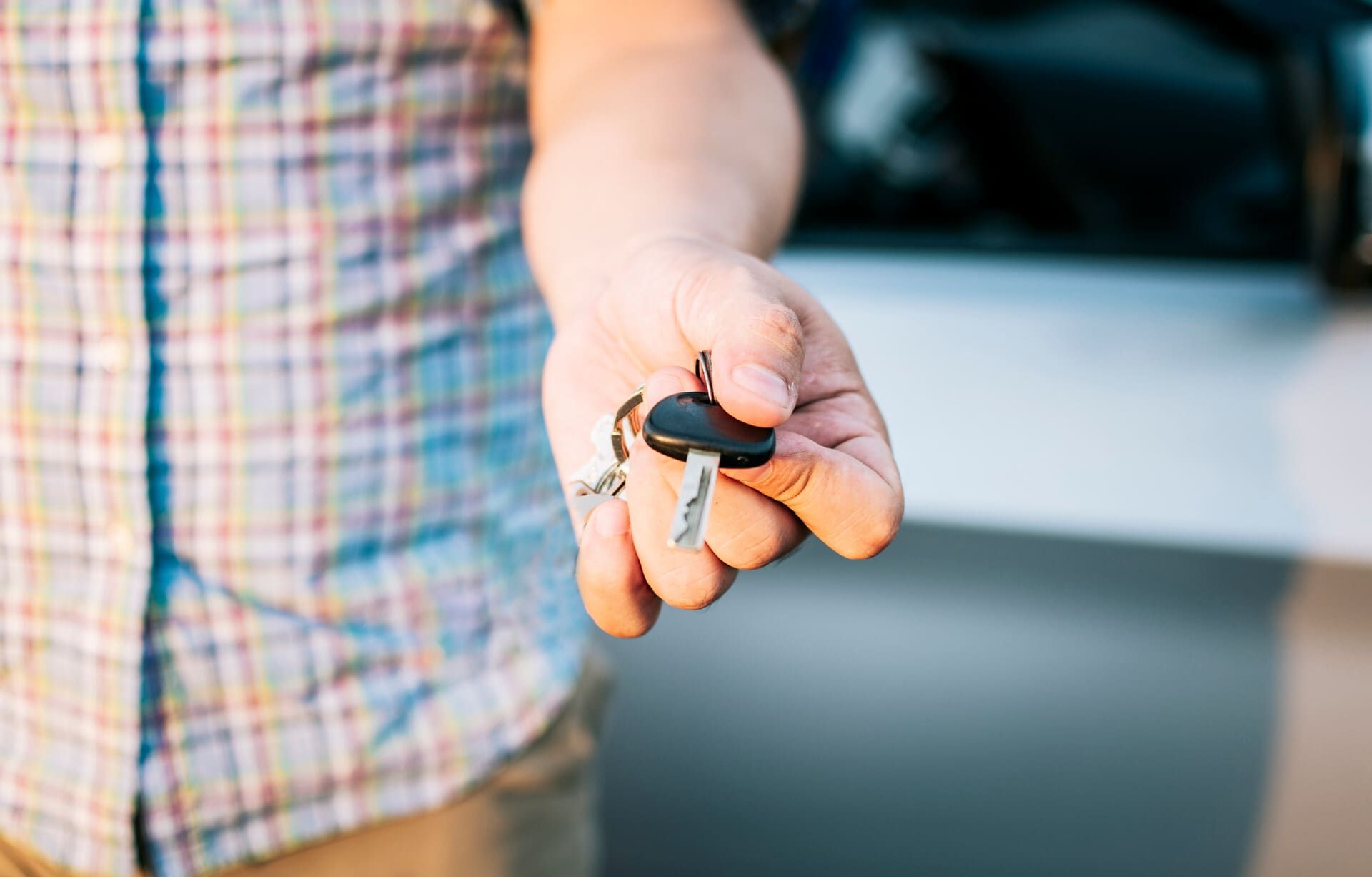 Un hombre sostiene una llave de coche en su mano delante de un coche.