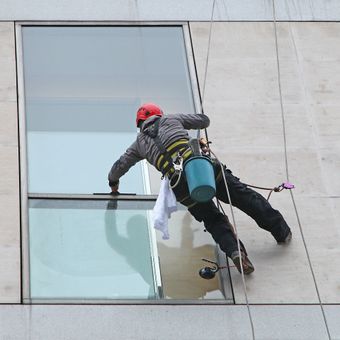 Agent d'entretien en plein nettoyage de vitres en extérieur, en suspension dans les airs