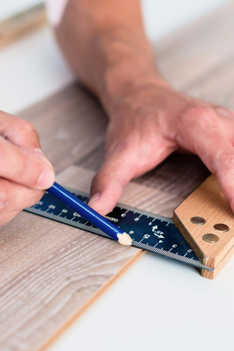 Eine Person misst ein Stück Holz mit einem Lineal und einem Bleistift.