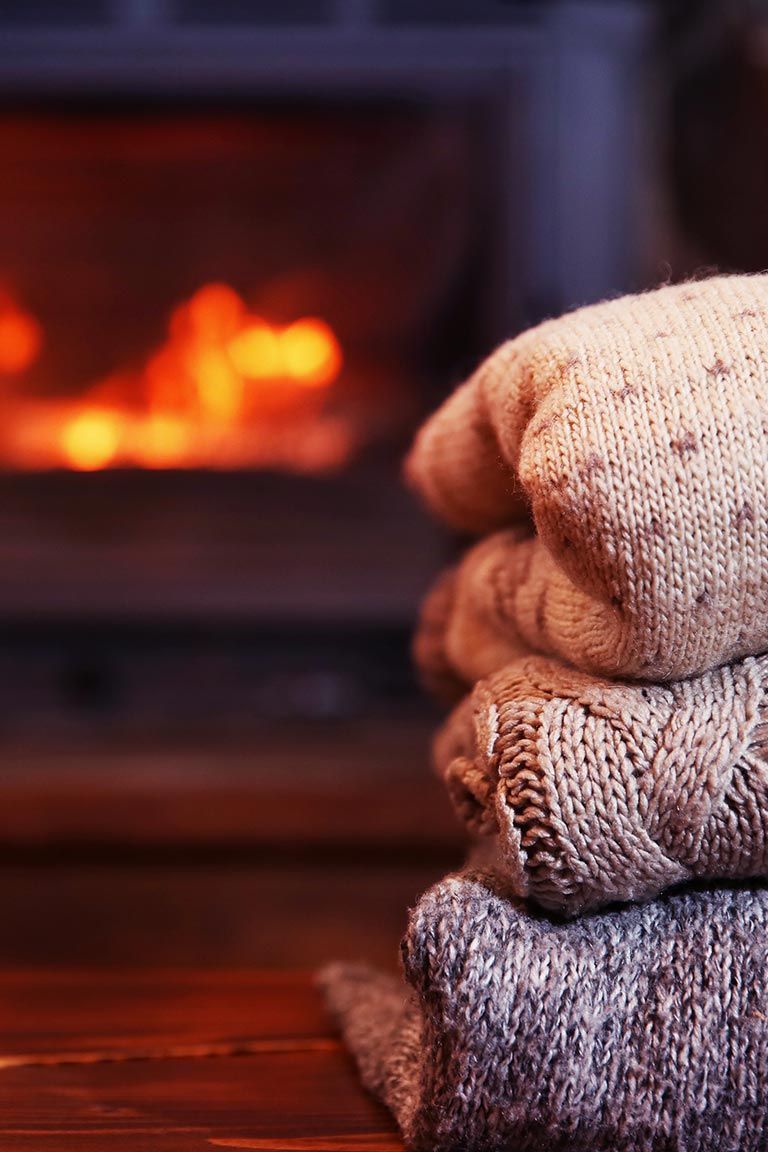 Ein Stapel Pullover liegt auf einem Holztisch vor einem Kamin.