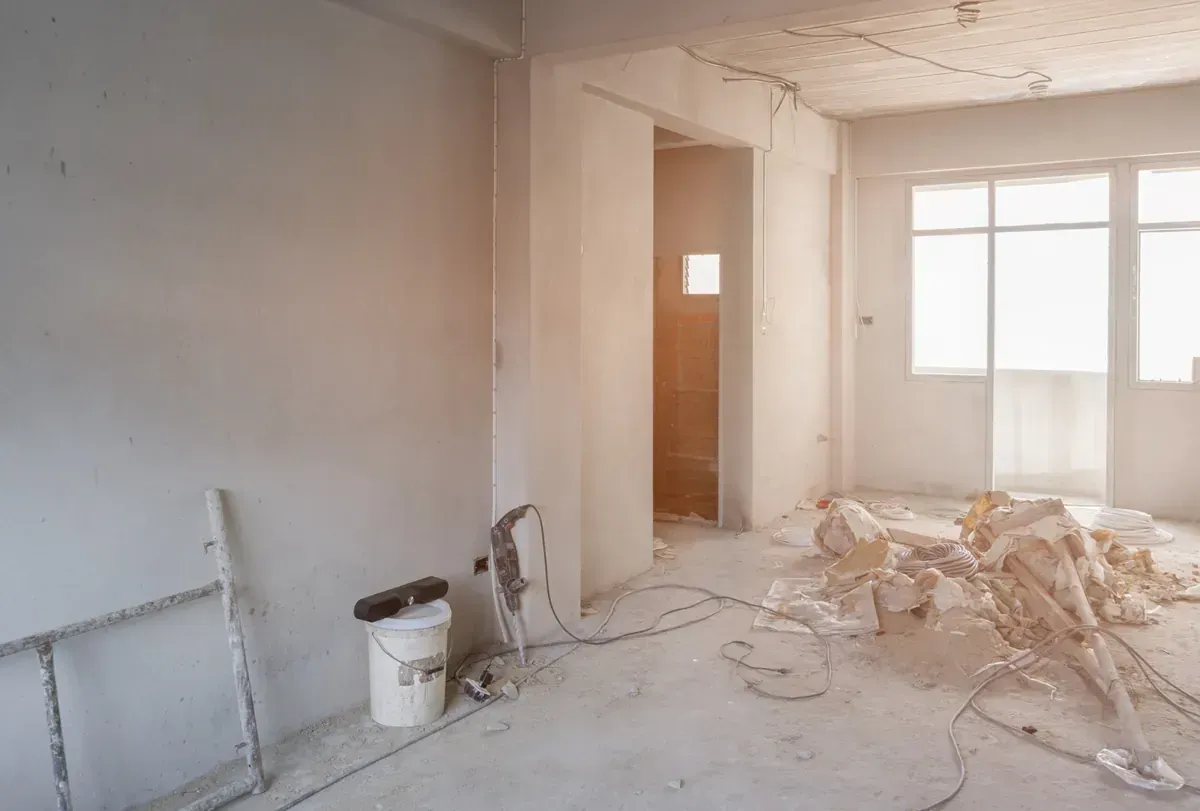 Interior de una habitación en construcción, con paredes expuestas, escombros en el piso y luz natural.