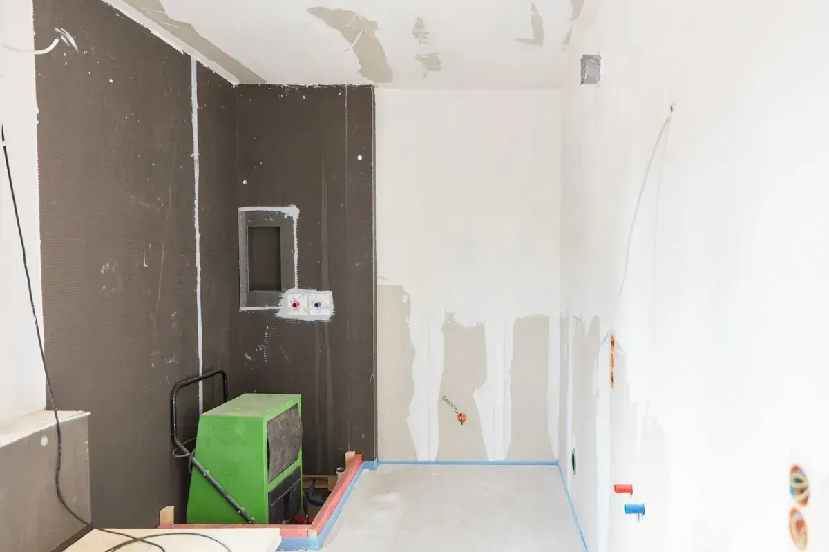 Habitación en construcción, con paredes grises y blancas, cableado y un deshumidificador verde.