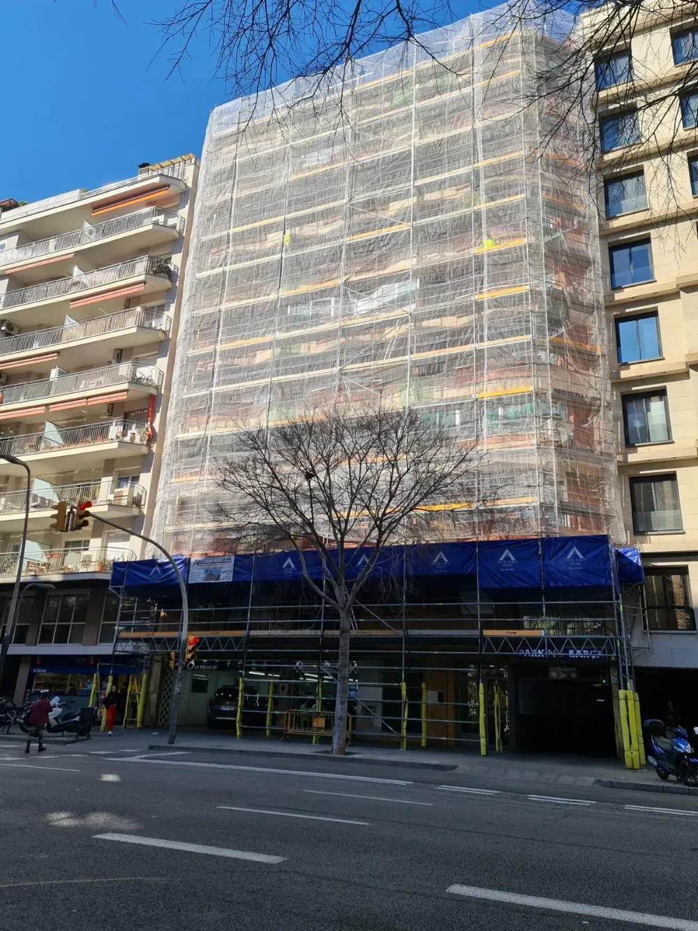 Dos limpiadores de ventanas con cuerdas limpian un edificio gris y blanco bajo un cielo azul claro.