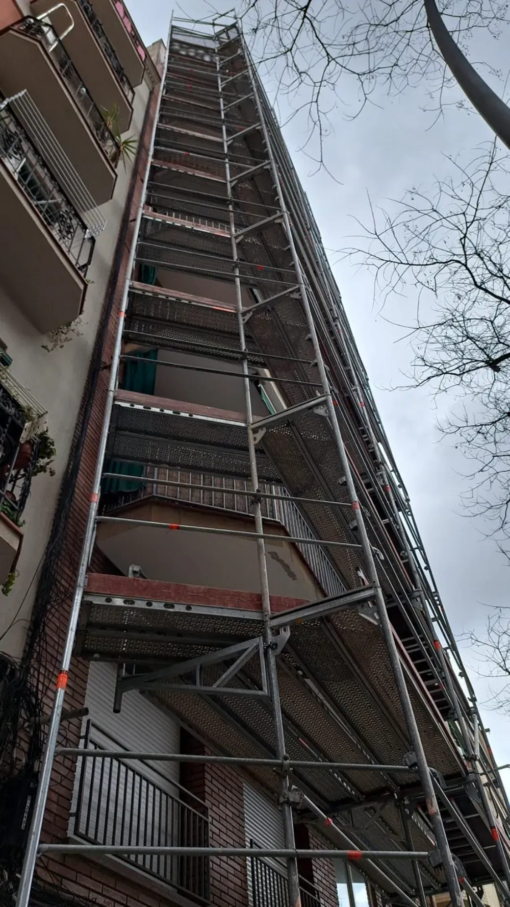 Trabajadores en una plataforma suspendida; aplicando mantenimiento a la fachada de un edificio alto y de color claro.