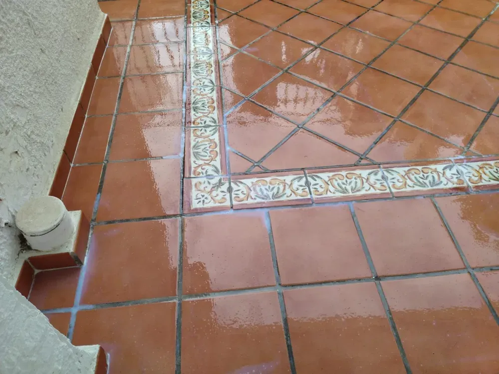 Interior de ático en reforma, con grandes ventanales, vigas de madera, escalera y restos de obra en el suelo.