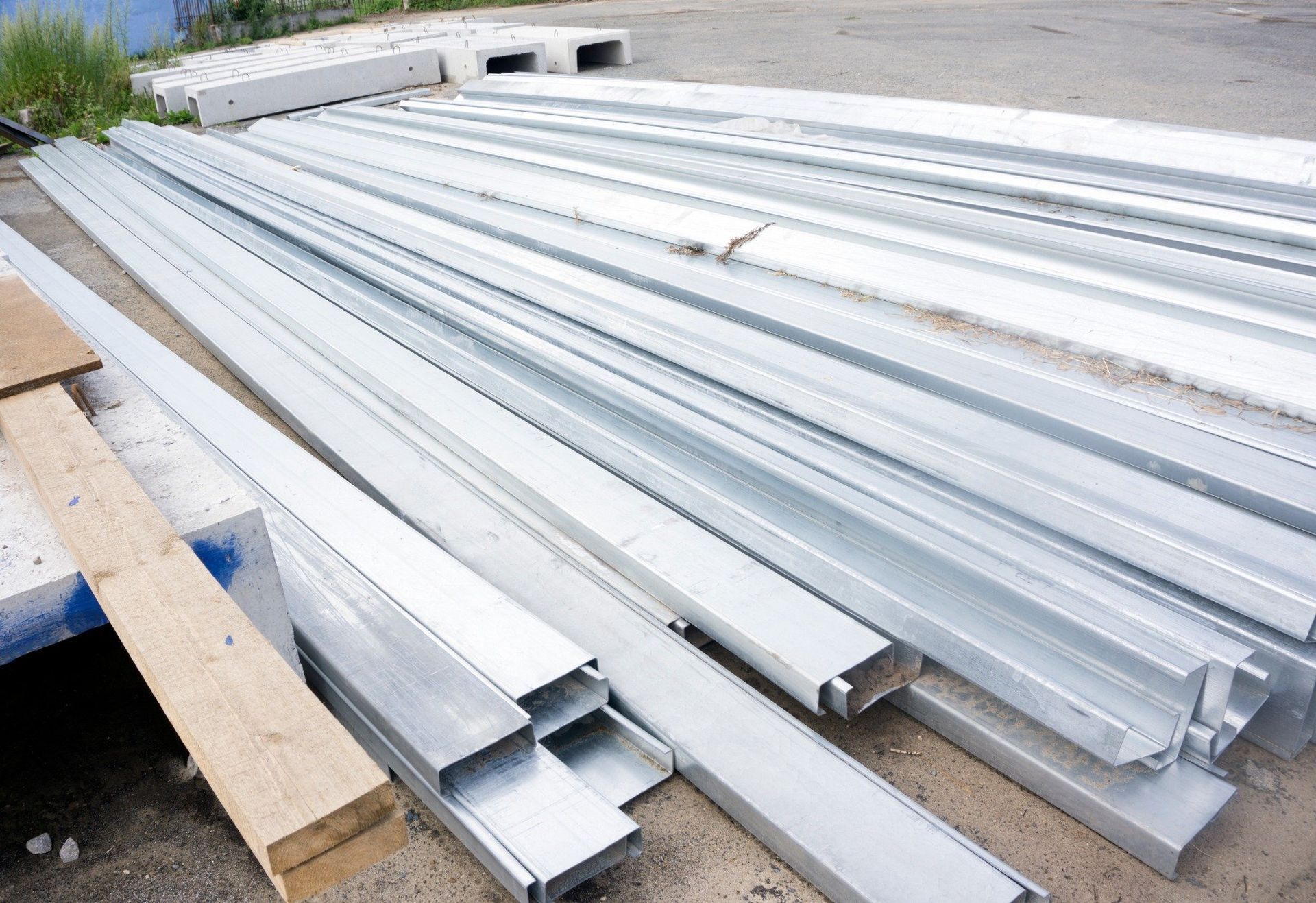 Vigas de canal de metal y madera apiladas al aire libre sobre una superficie de hormigón.