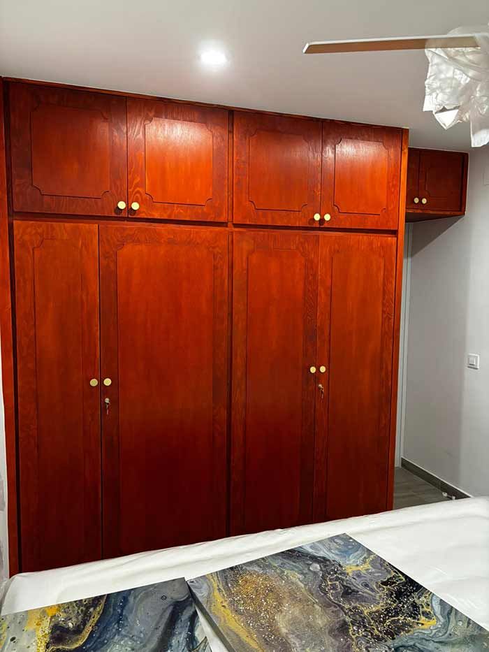 Gran armario empotrado de madera con múltiples puertas y un pequeño compartimento separado contra una pared blanca.