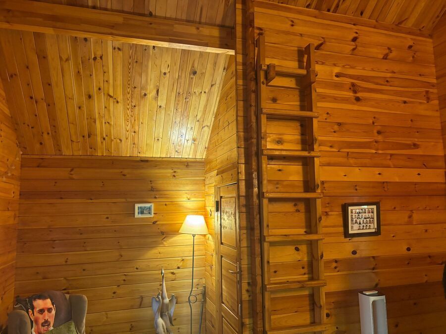 Interior revestido con paneles de madera y una escalera que conduce al nivel superior. Se ven una lámpara de pie y obras de arte.