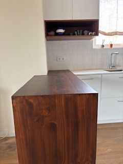 Isla de cocina de madera oscura con gabinetes blancos, estante y ventana en el fondo.