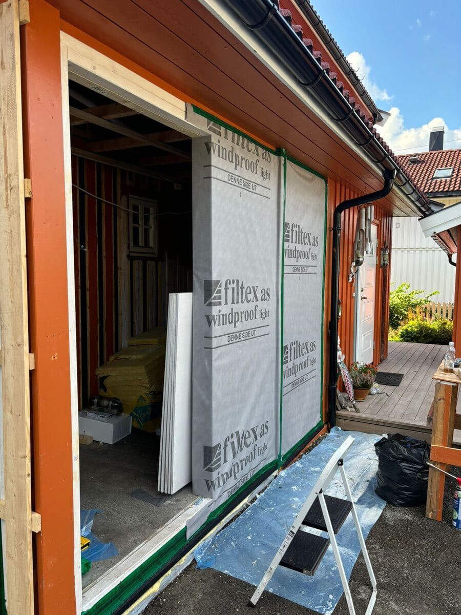 Exterior de un edificio en construcción, con paneles de pared aislantes y una puerta parcialmente enmarcada. Se aprecian molduras naranjas y verdes.