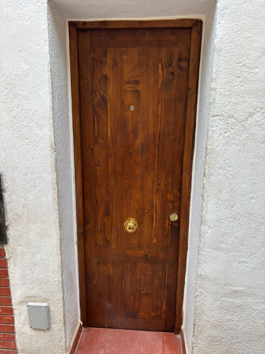Puerta de madera empotrada en pared blanca con pomo de latón.
