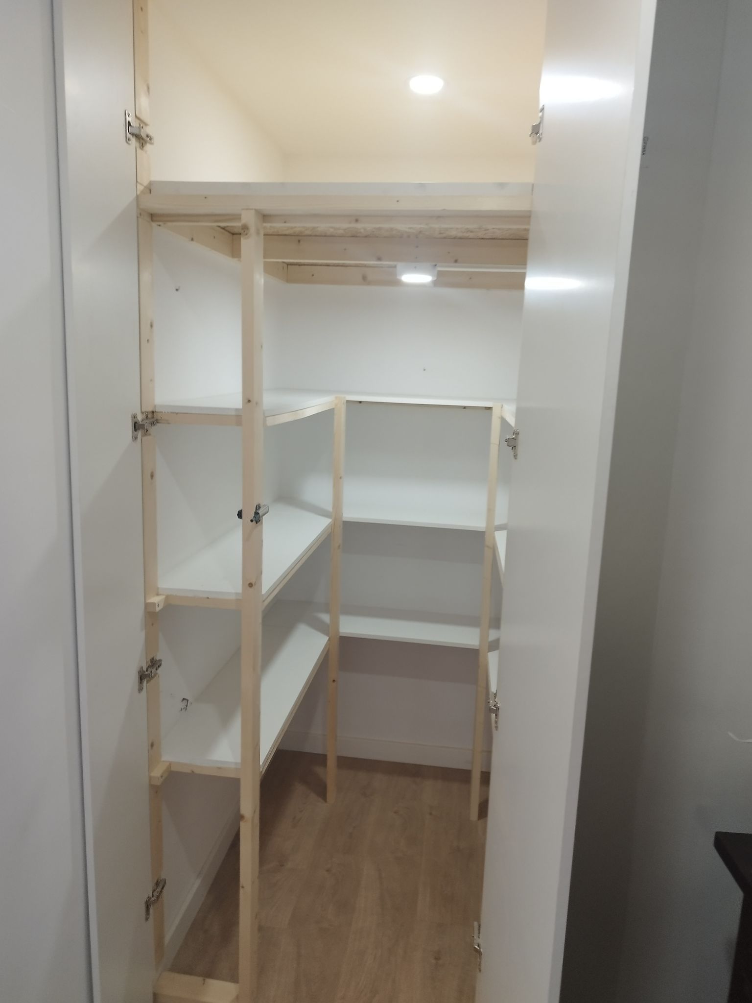 Despensa blanca con estantes de madera, vista desde el interior con las puertas abiertas.