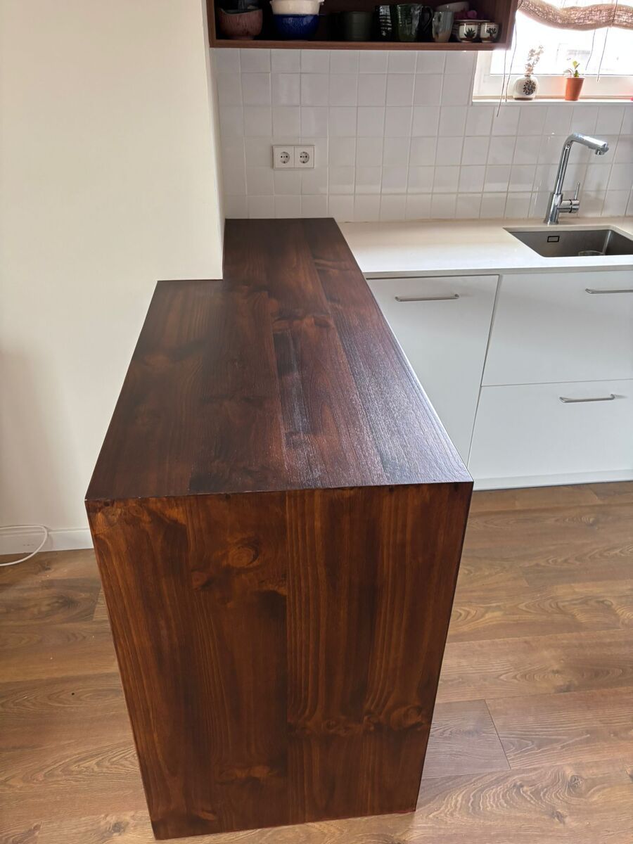 Isla de cocina de madera teñida oscura contra gabinetes blancos y pared de azulejos.