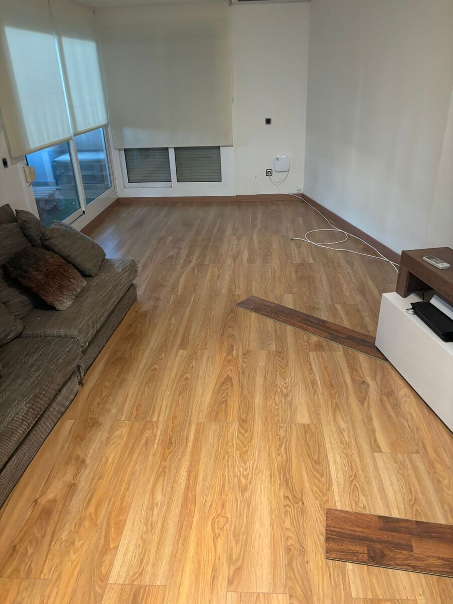 Habitación con nuevo piso imitación madera instalado; se ven un sofá, una ventana y una pared.