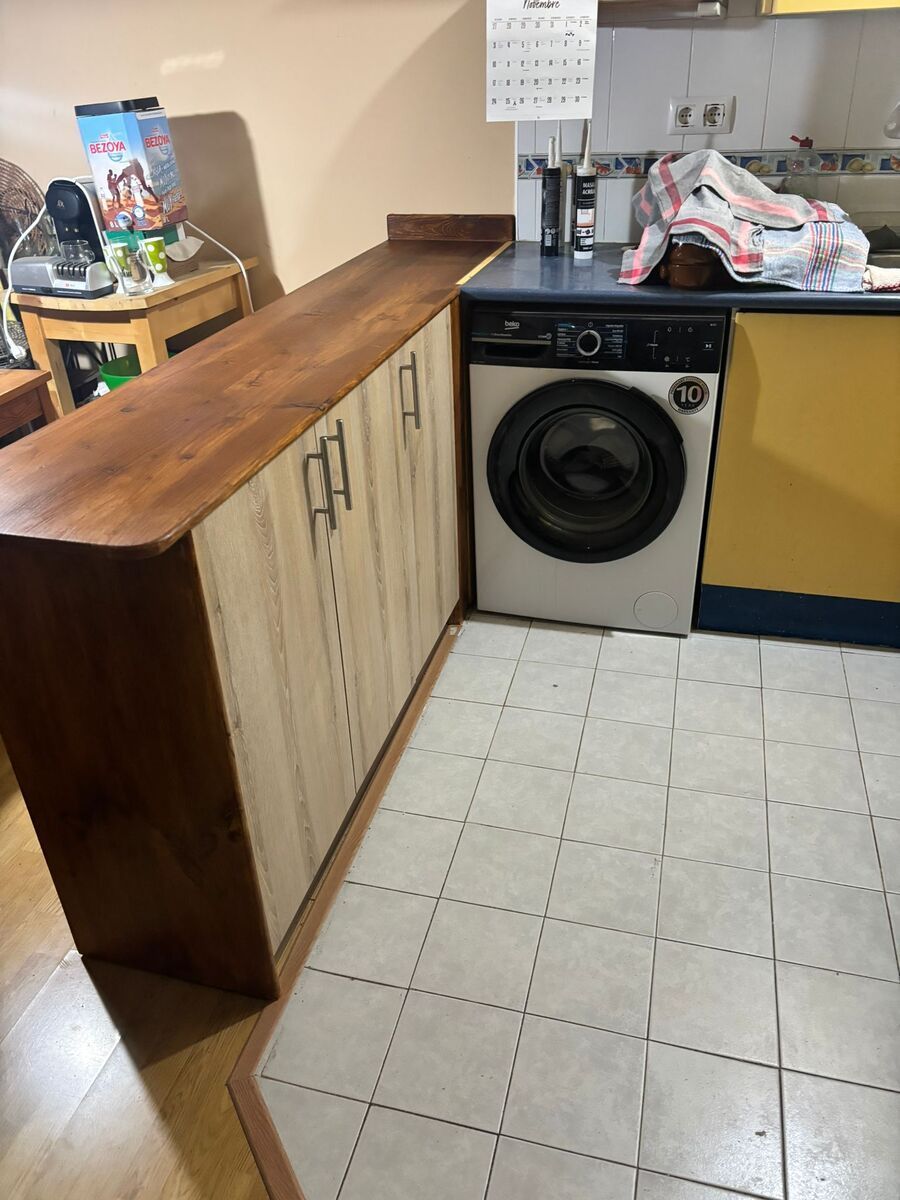 Una cocina con lavadora y armarios. Los armarios son de madera clara y la encimera es de madera oscura.