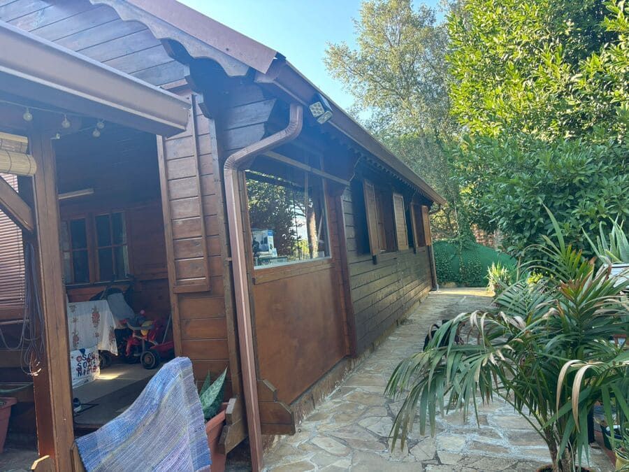 Exterior de cabaña de madera con paredes marrones, canaletas y exuberante vegetación al fondo.