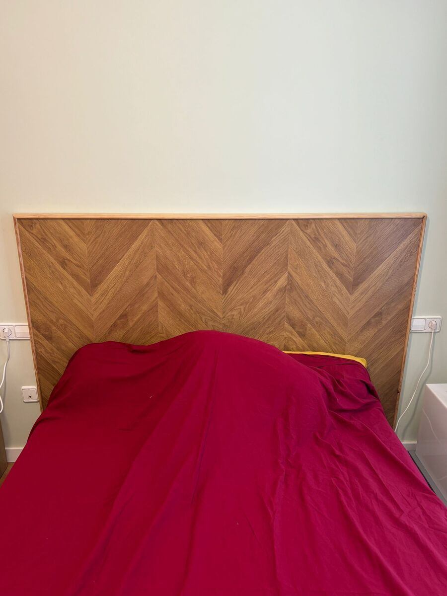 Cabecero de madera con manta roja sobre una cama, contra una pared verde claro.