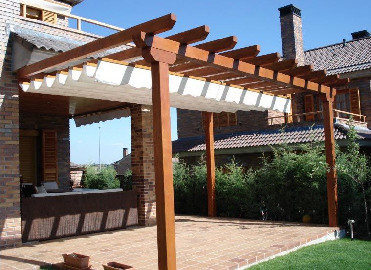 Pérgola de madera con tela de sombra blanca sobre un patio de ladrillo.