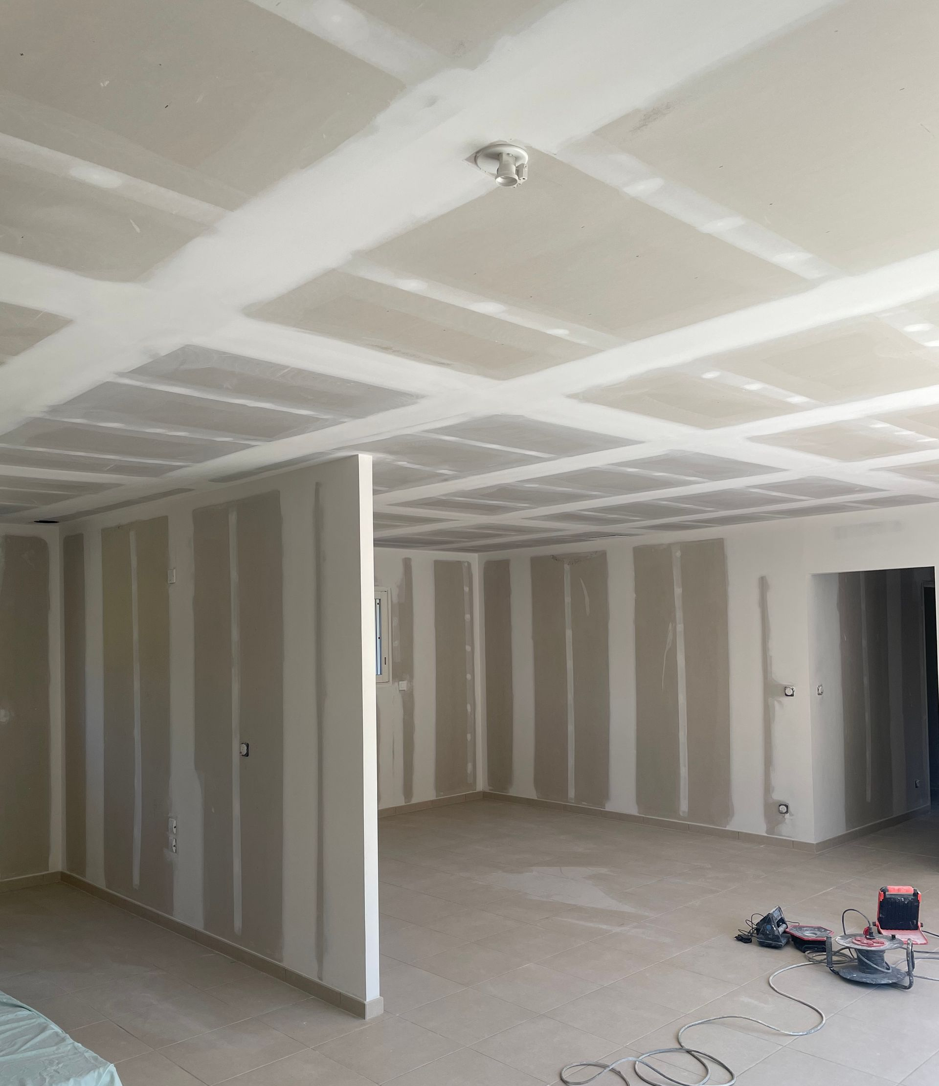 Une pièce intérieure en construction avec des plaques de plâtre nouvellement installées au plafond et aux murs, laissant apparaître les joints.