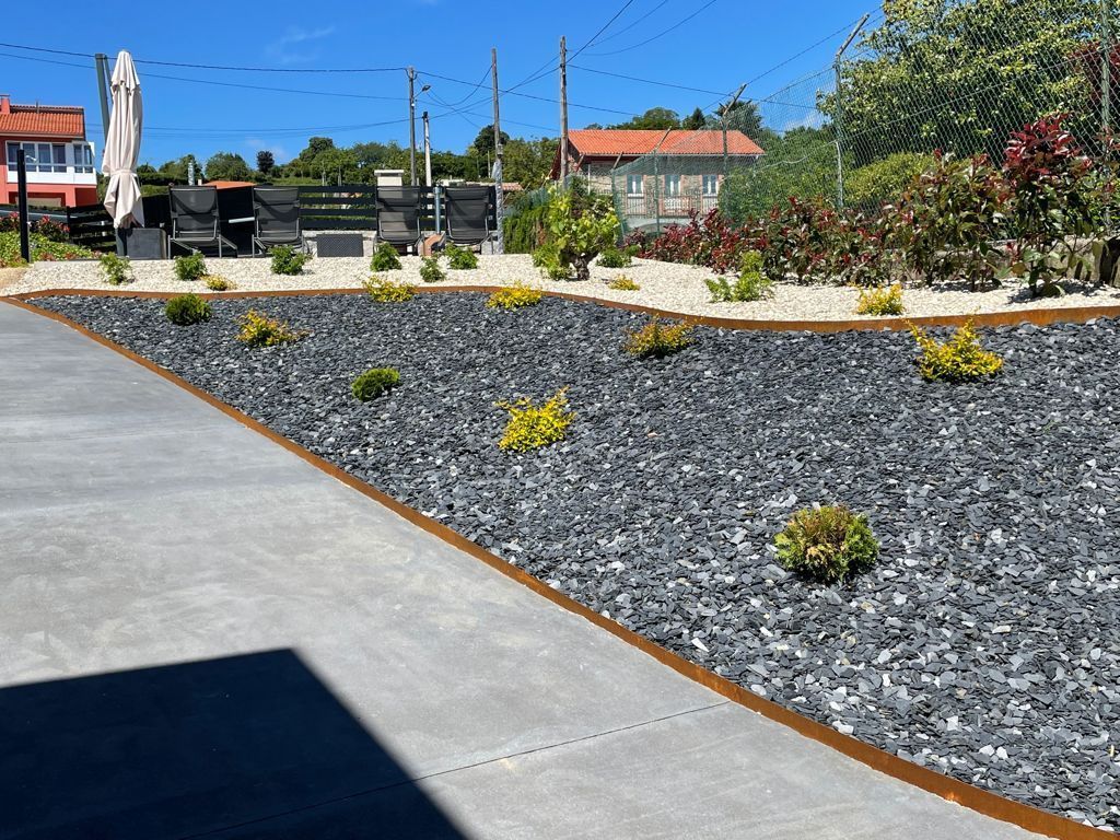 Un jardín de grava con una pasarela de hormigón y una casa al fondo.