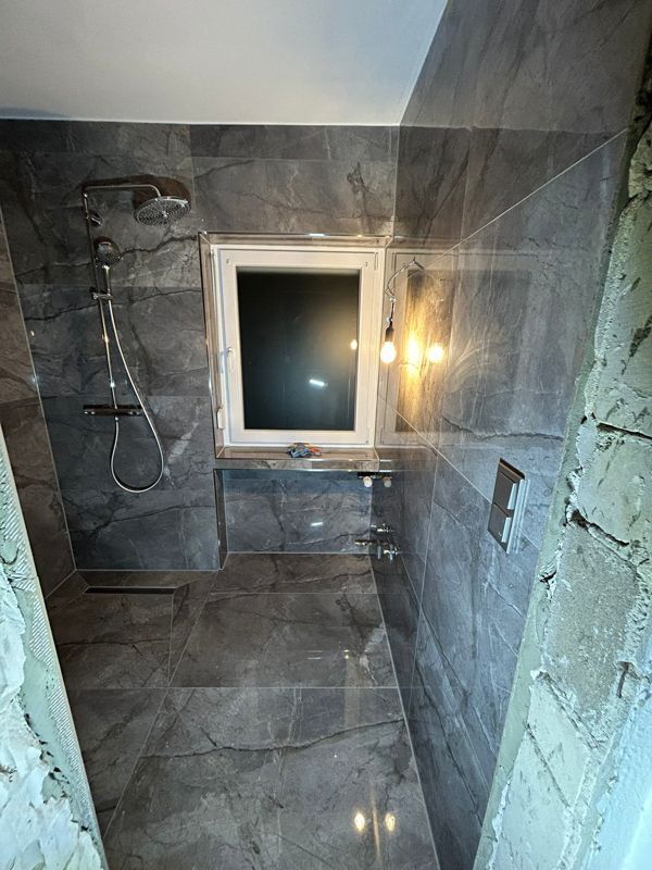 Ein Badezimmer mit grauen Fliesen und einem Fenster.