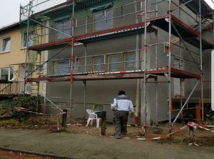 Ein Mann steht vor einem Gebäude, das von einem Gerüst umgeben ist.