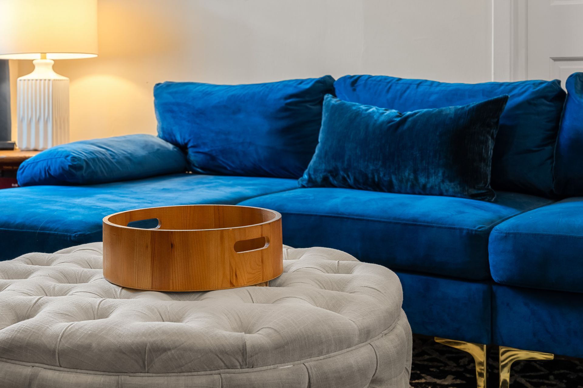 Blue velvet sectional sofa with a round ottoman and wooden tray.