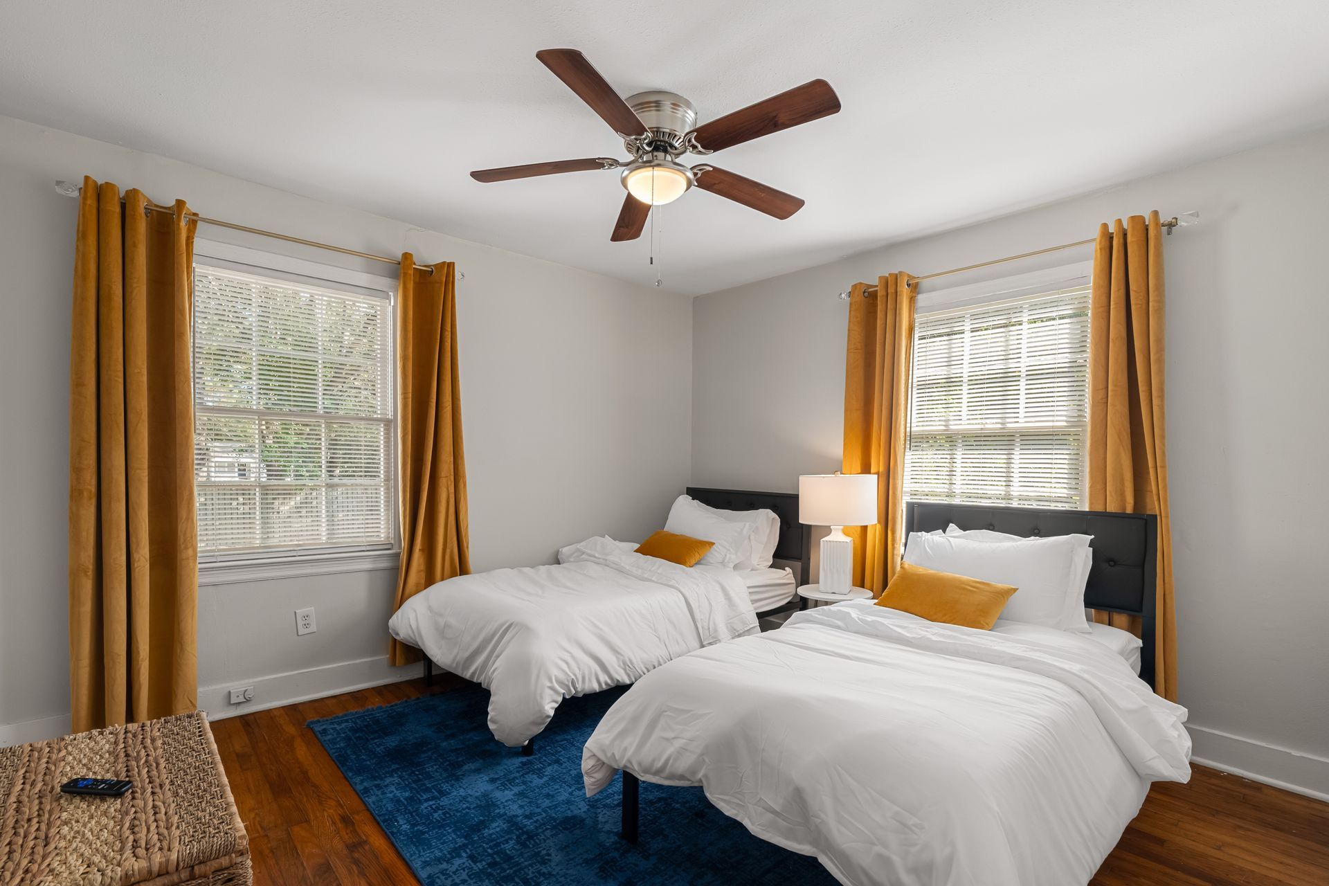 Bedroom with two twin beds, blue rug, and mustard yellow curtains.