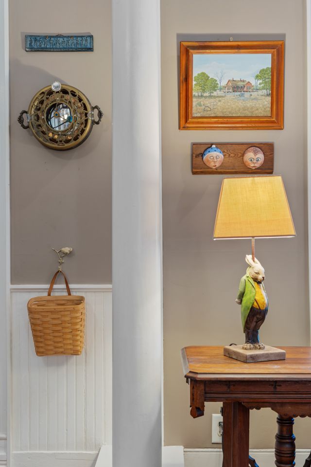 Interior with art and decor on a wall; a lamp with parrot base sits on a table.