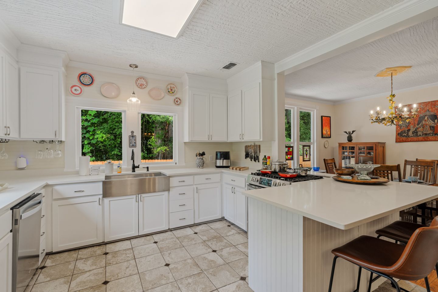White kitchen with stainless steel sink, island with seating, and view into dining room.