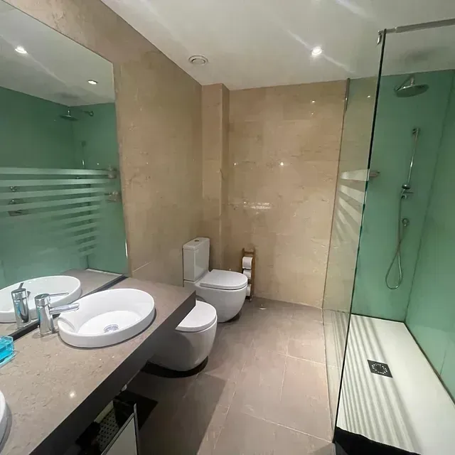 Un baño con dos lavabos, un inodoro y una ducha a ras de suelo.