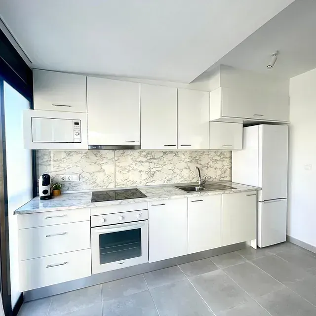 Una cocina con gabinetes blancos, un refrigerador, un fregadero y un microondas.