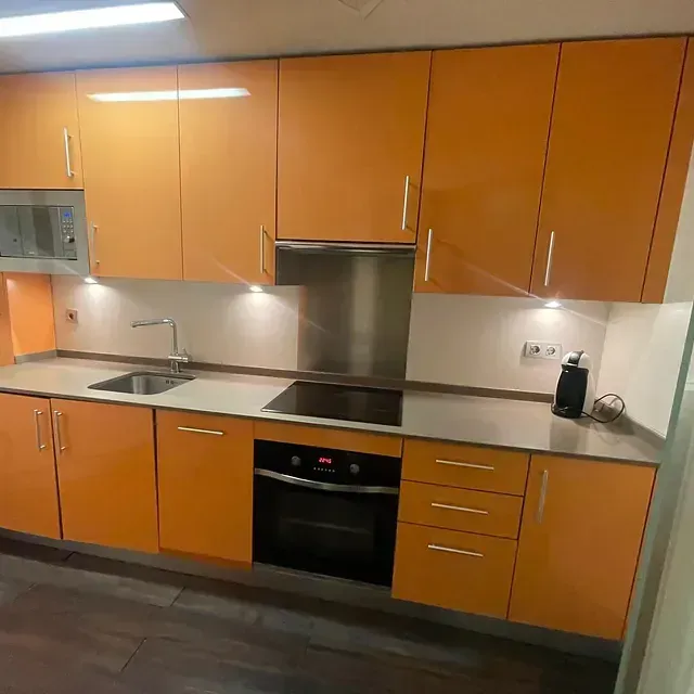 Una cocina con gabinetes naranjas y electrodomésticos de acero inoxidable.