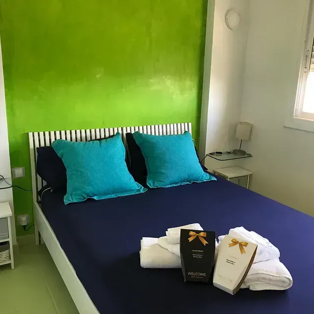 Una cama con almohadas azules y una pared verde.