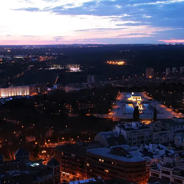 Una vista aérea de una ciudad de noche con una puesta de sol de fondo.