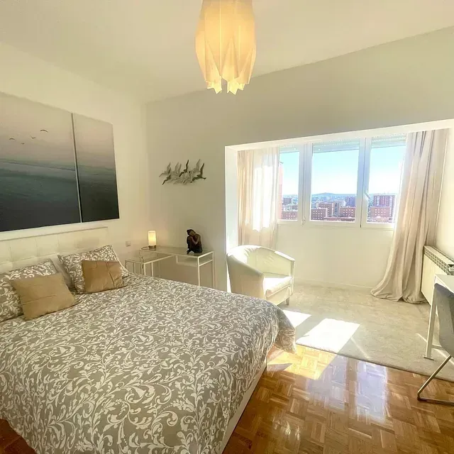 Un dormitorio con cama, silla, escritorio y ventana.