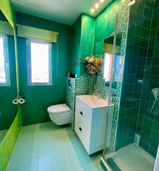 Un baño con azulejos verdes, inodoro, lavabo y ducha.